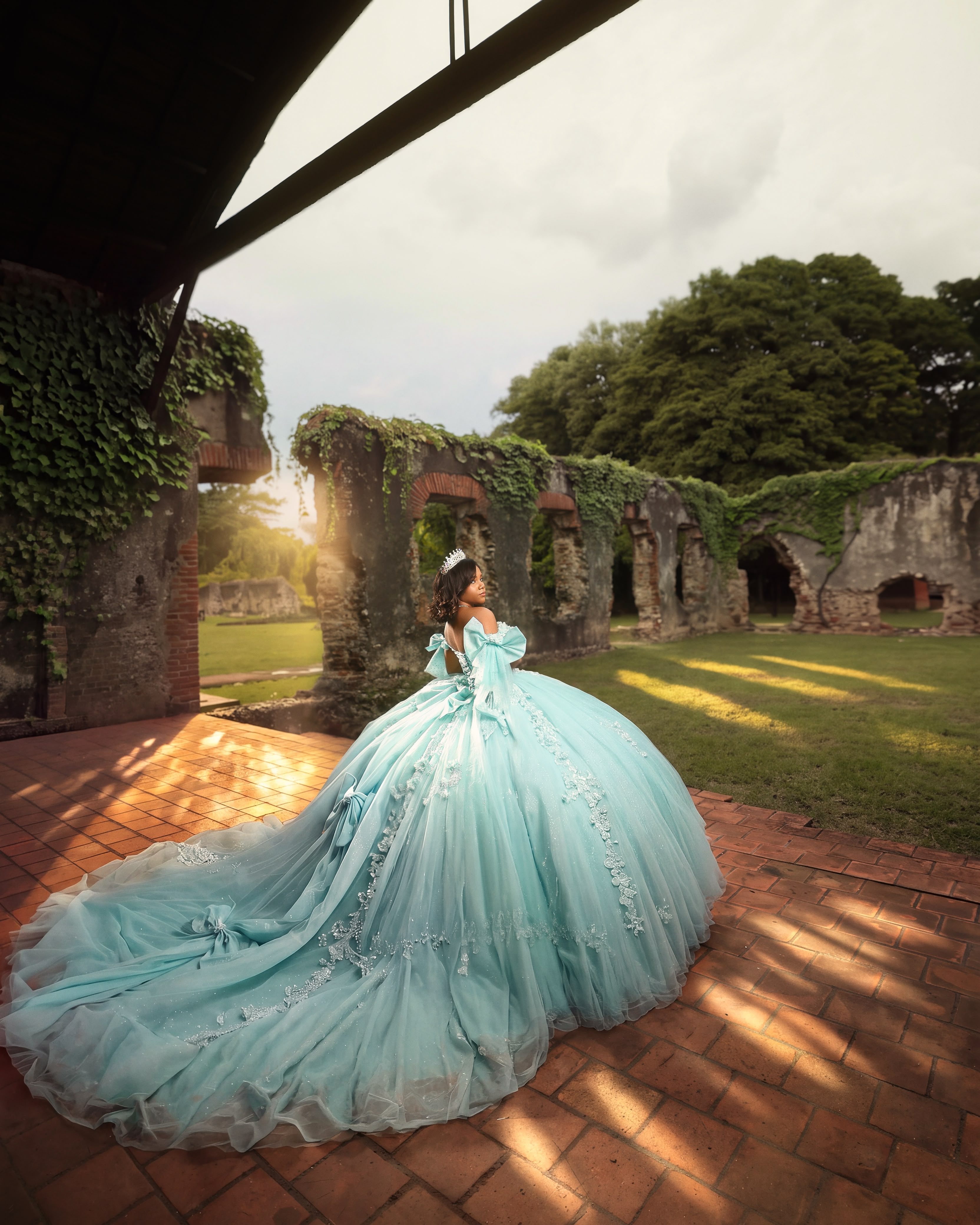 Quinceañera con vestido verde menta entre ruinas cubiertas de hiedra y un jardín al sol
