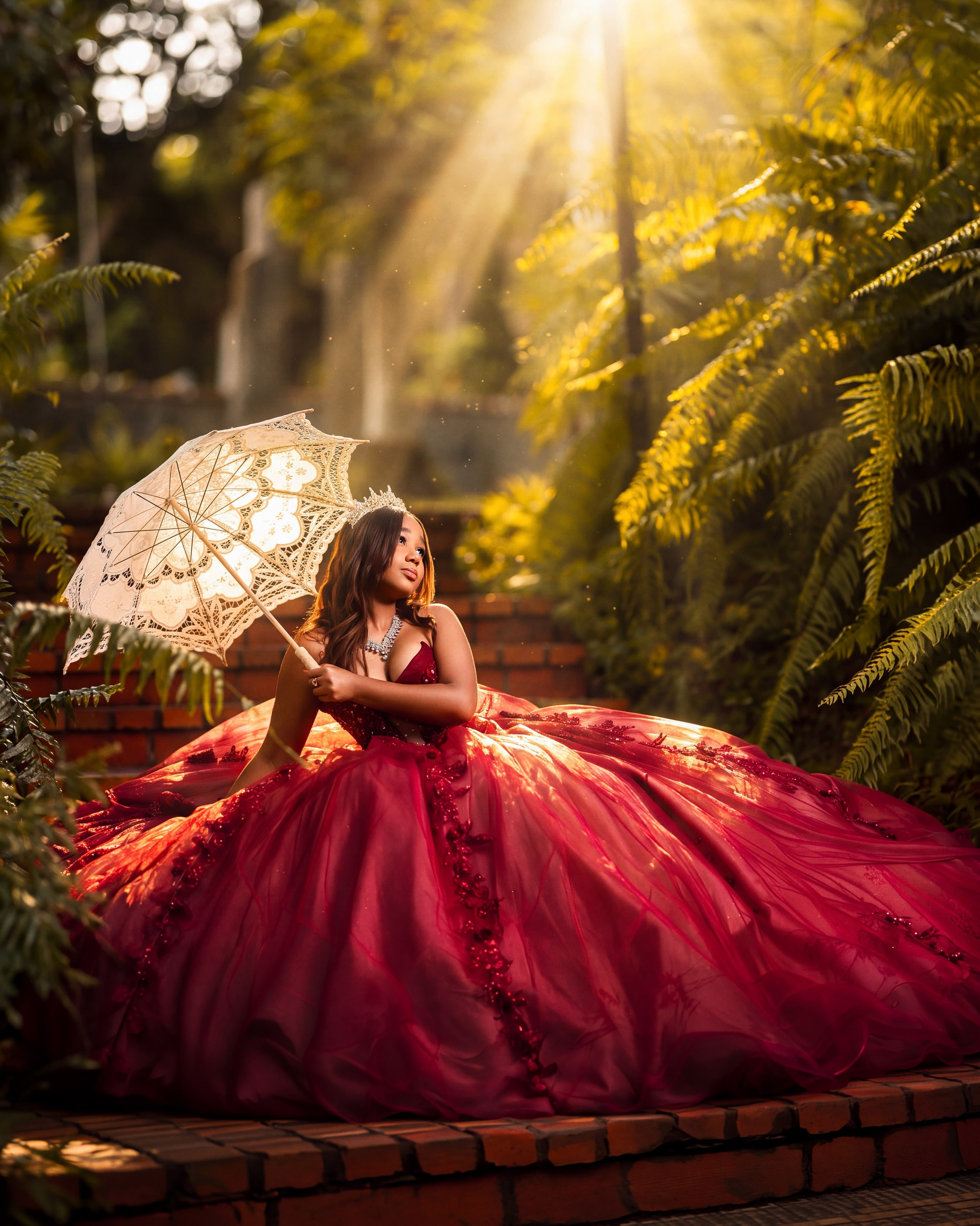Quinceañera con vestido rojo y sombrilla de encaje sentada entre helechos con rayos de sol