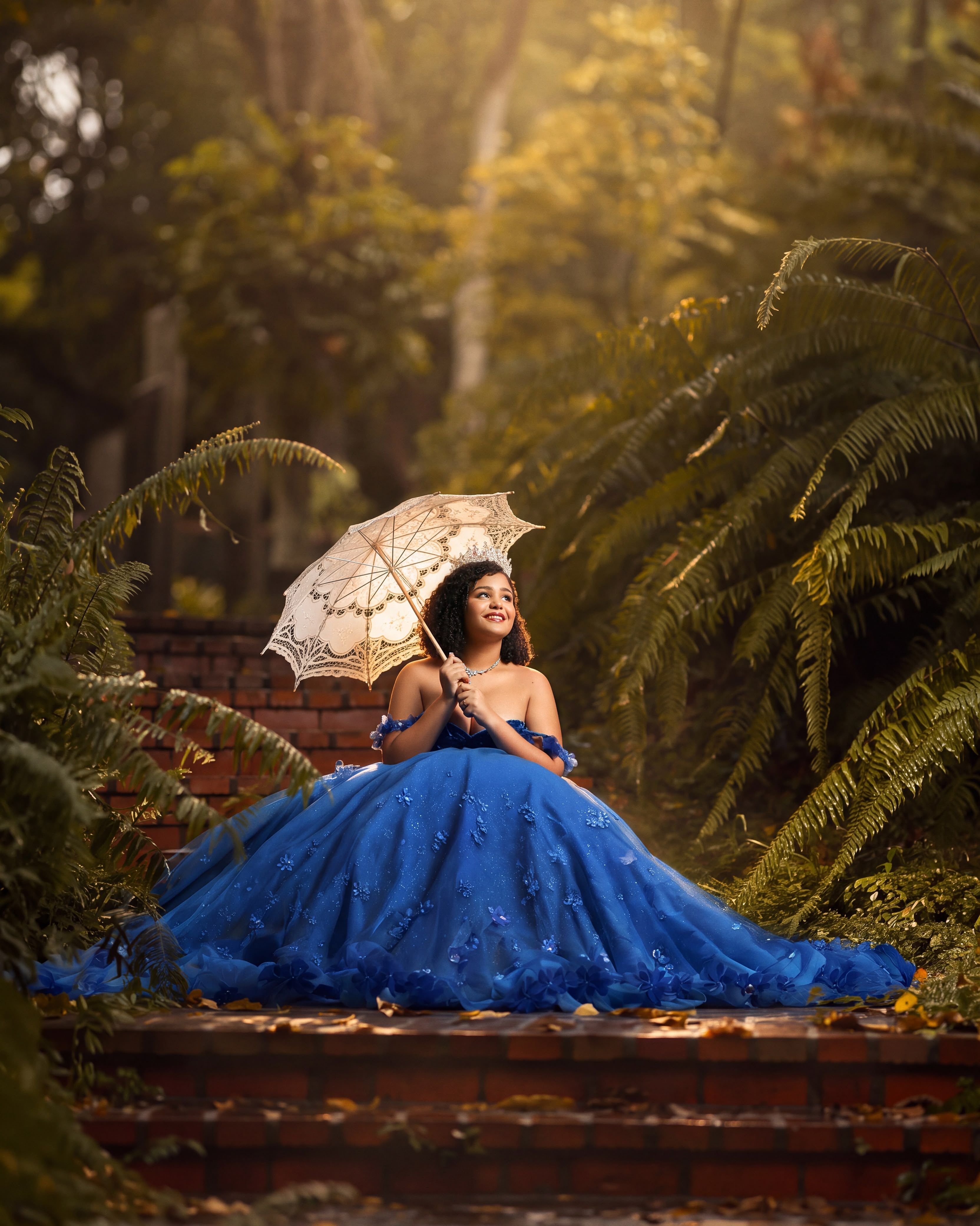 Quinceañera con vestido azul real y sombrilla de encaje en un jardín tropical