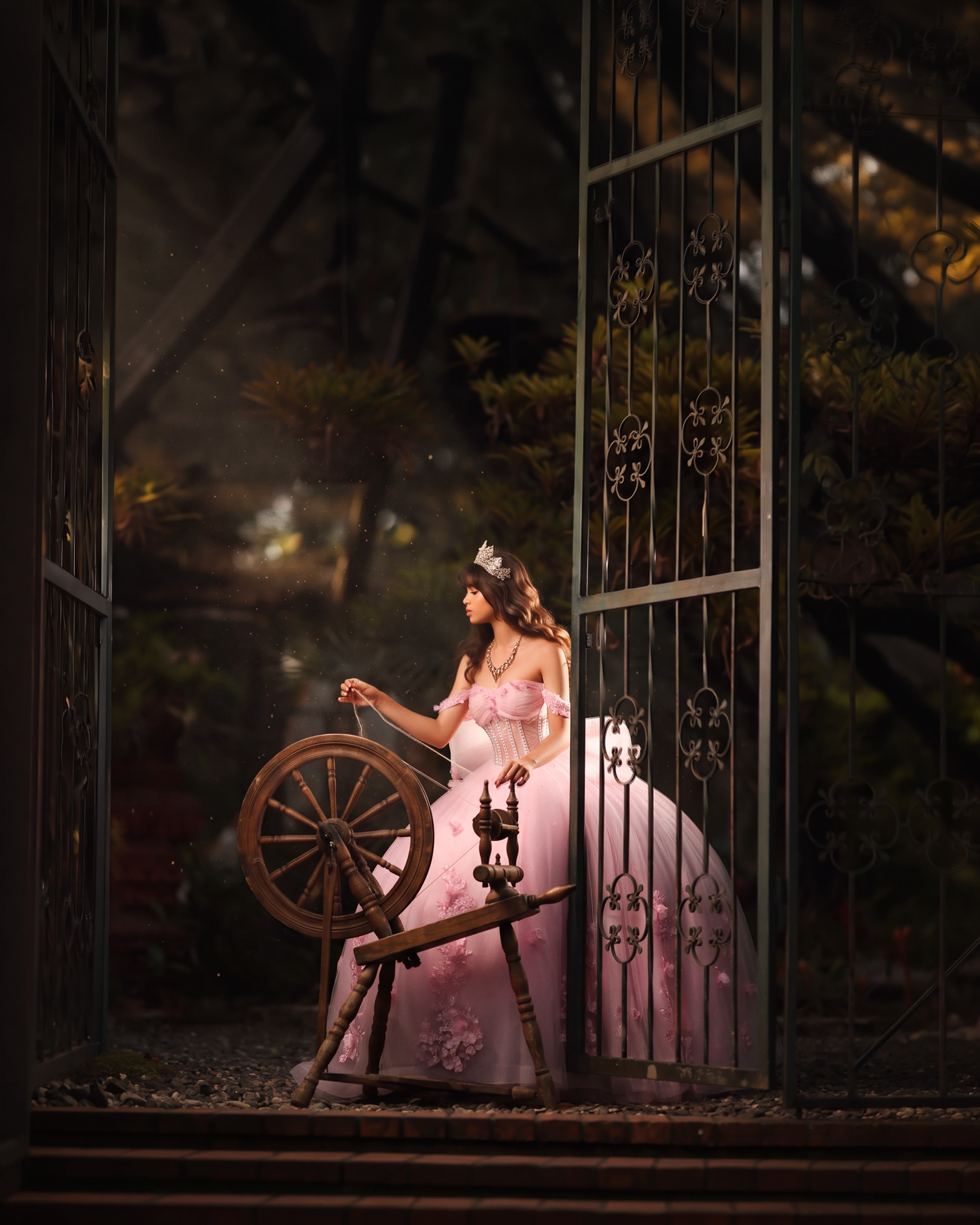 Quinceañera con vestido rosa junto a una rueca y una reja de hierro, como en un cuento de hadas