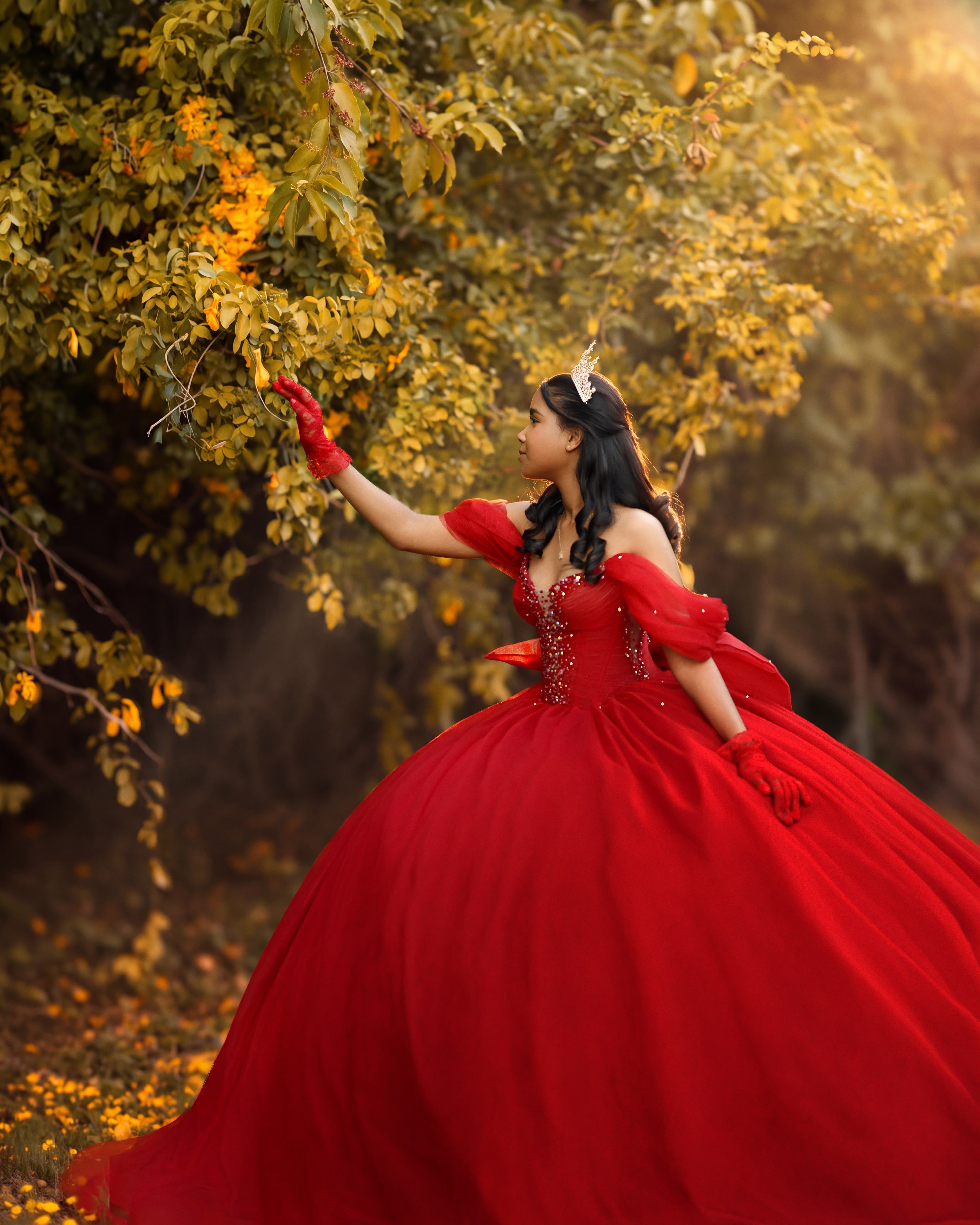 Quinceañera con vestido y guantes rojos alcanzando hojas doradas