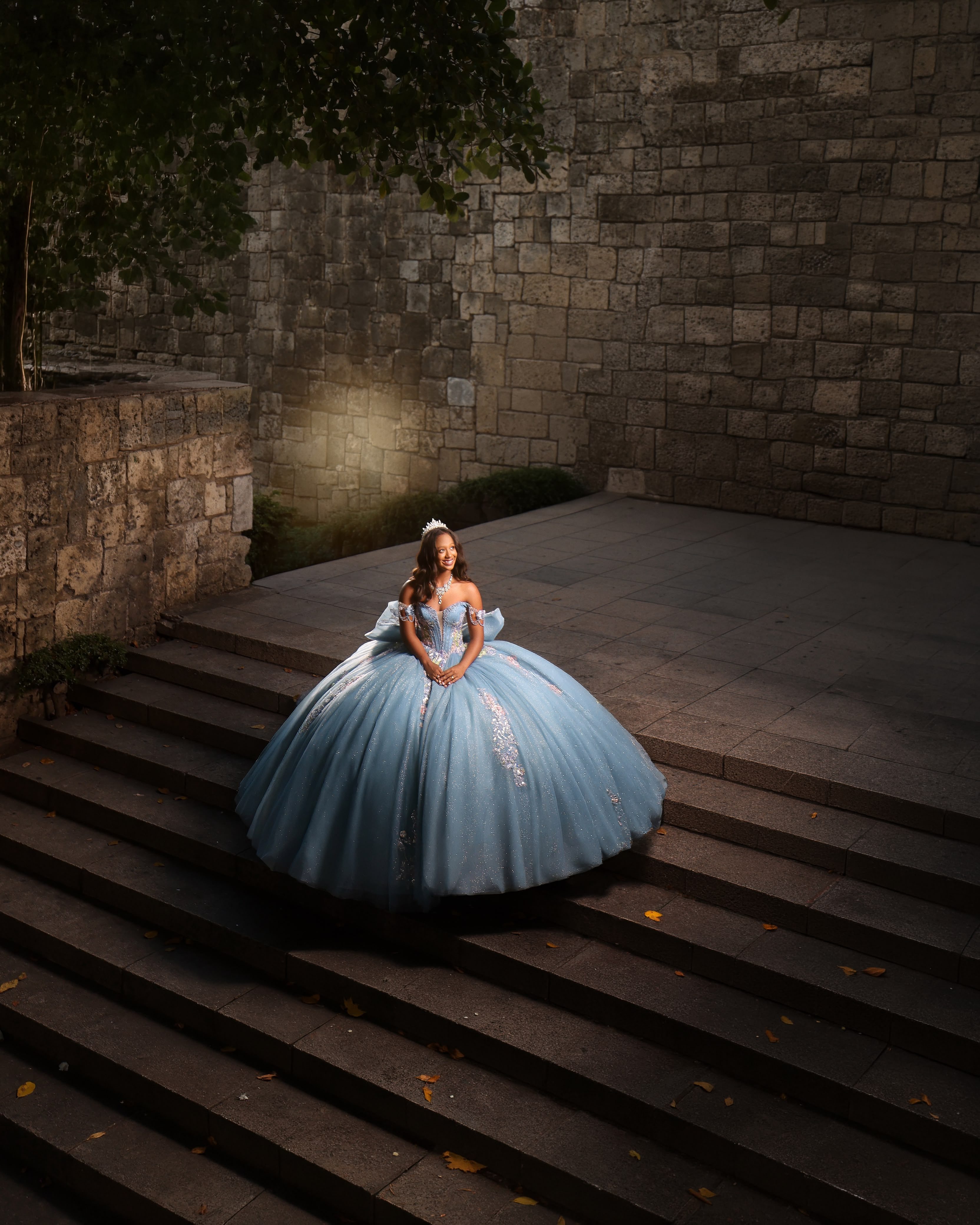 Quinceañera con vestido celeste sentada en una escalinata de piedra al anochecer